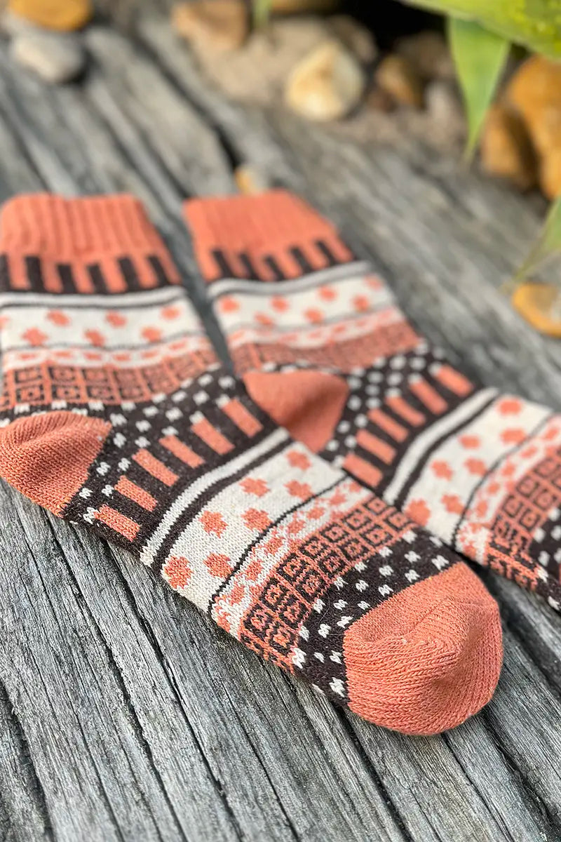 Nordic Style Socks in Burnt Orange Cross by Mabel + Meg laying on driftwood in the garden