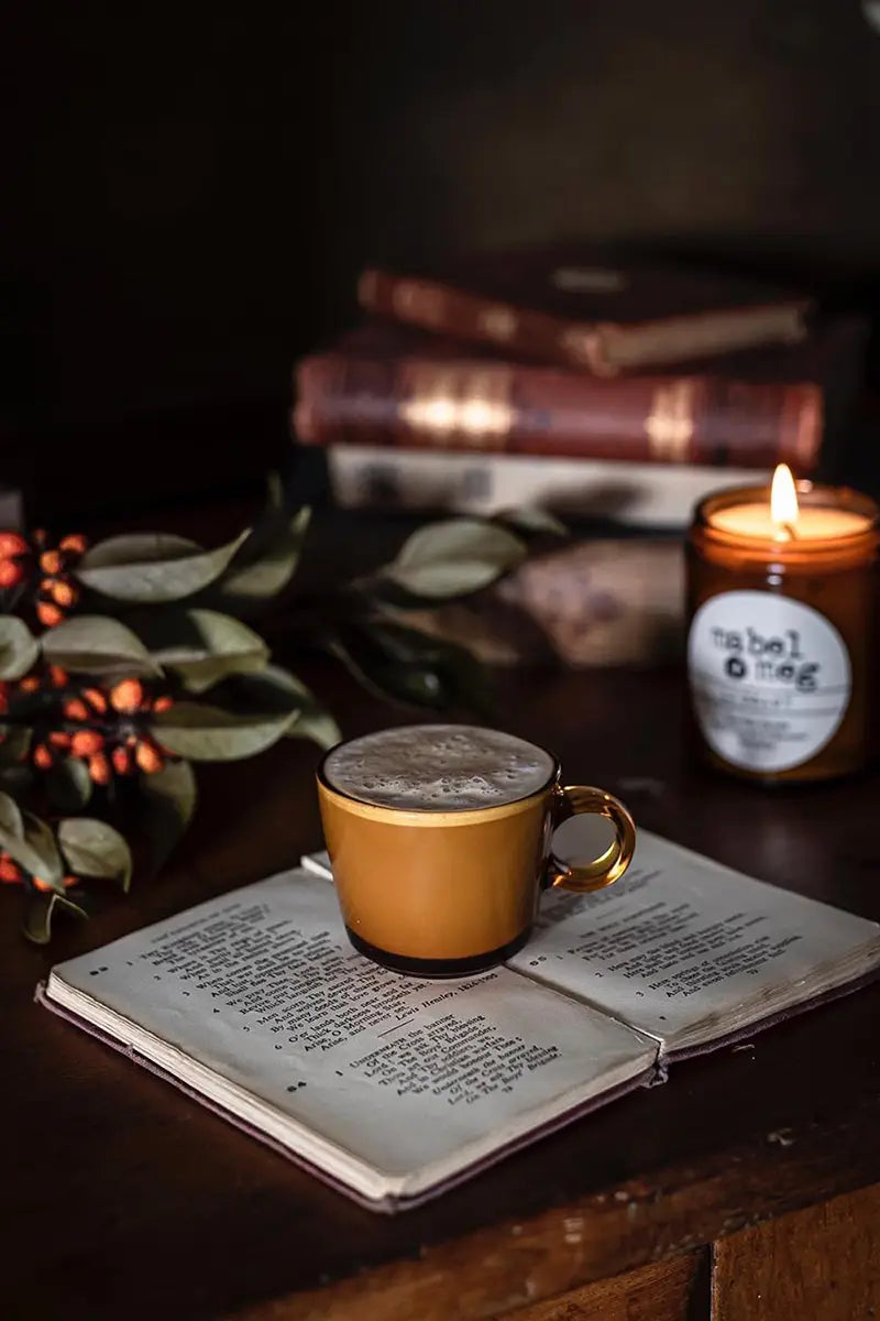 Scented Candle by Mabel + Meg in Christmas Pudding on a table with a book and lovely coffee.